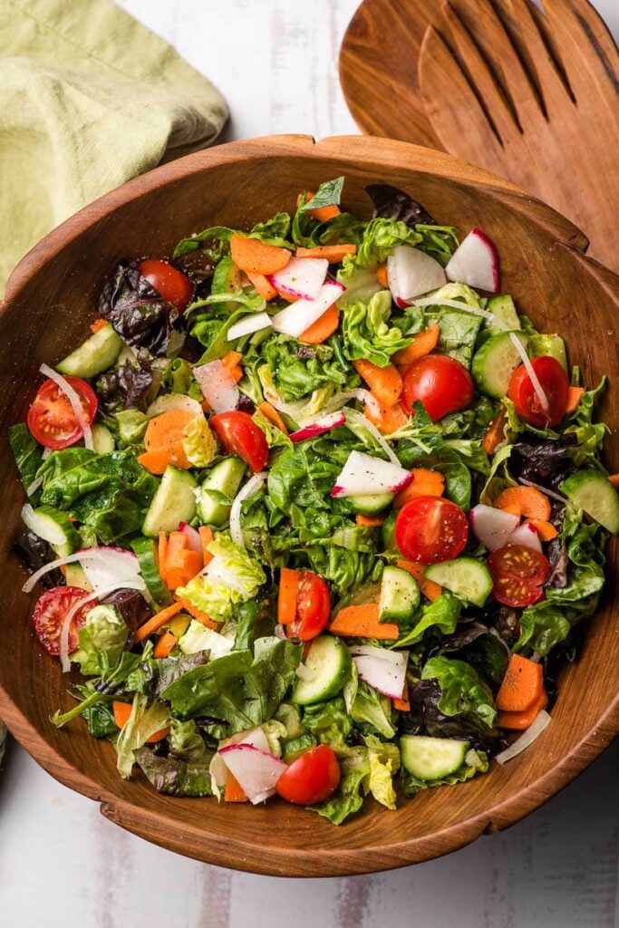 Wooden bamboo salad bowl filled with a garden salad and salad tongs sitting next to the bowl. 