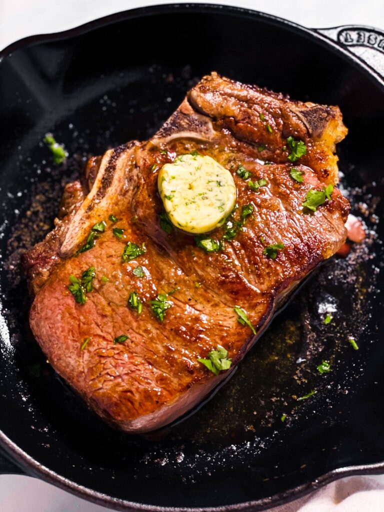 Steak in a cast iron pan with melting butter on top. 