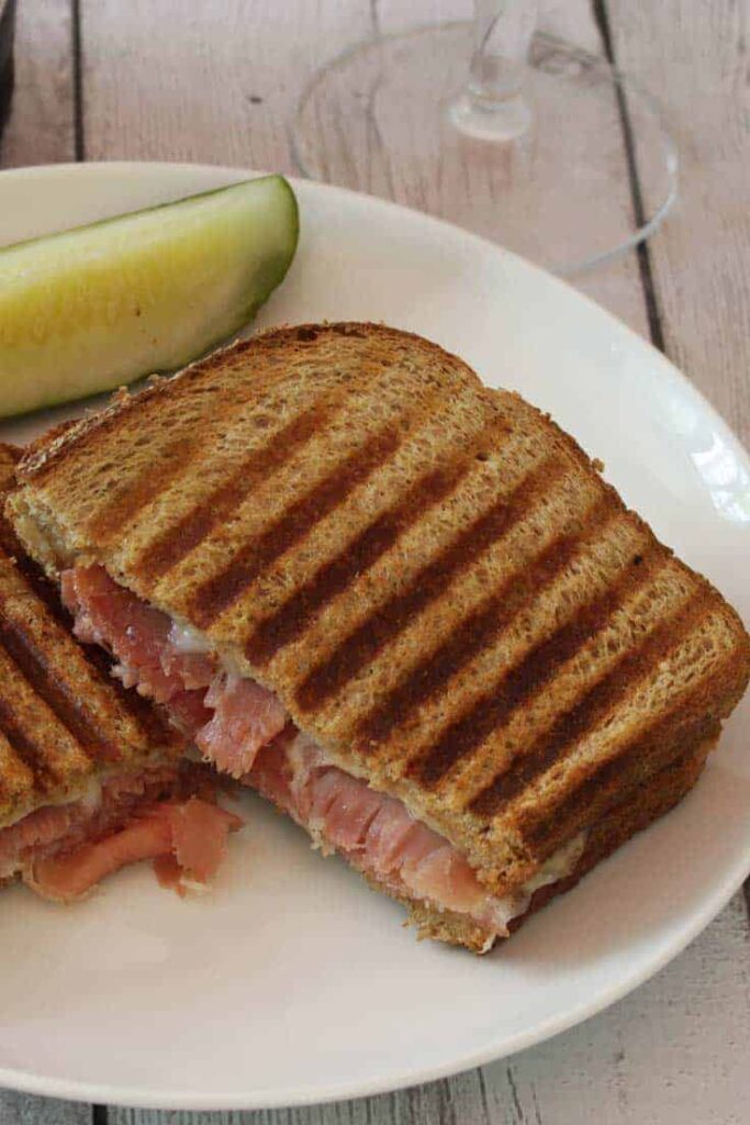 Serrano ham panini on a plate, cut in half with a pickle spear. 