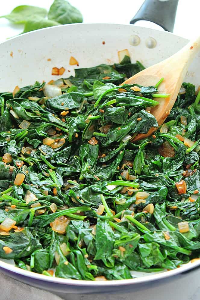 Bowl of sauteed spinach with a wooden spoon tucked into it. 