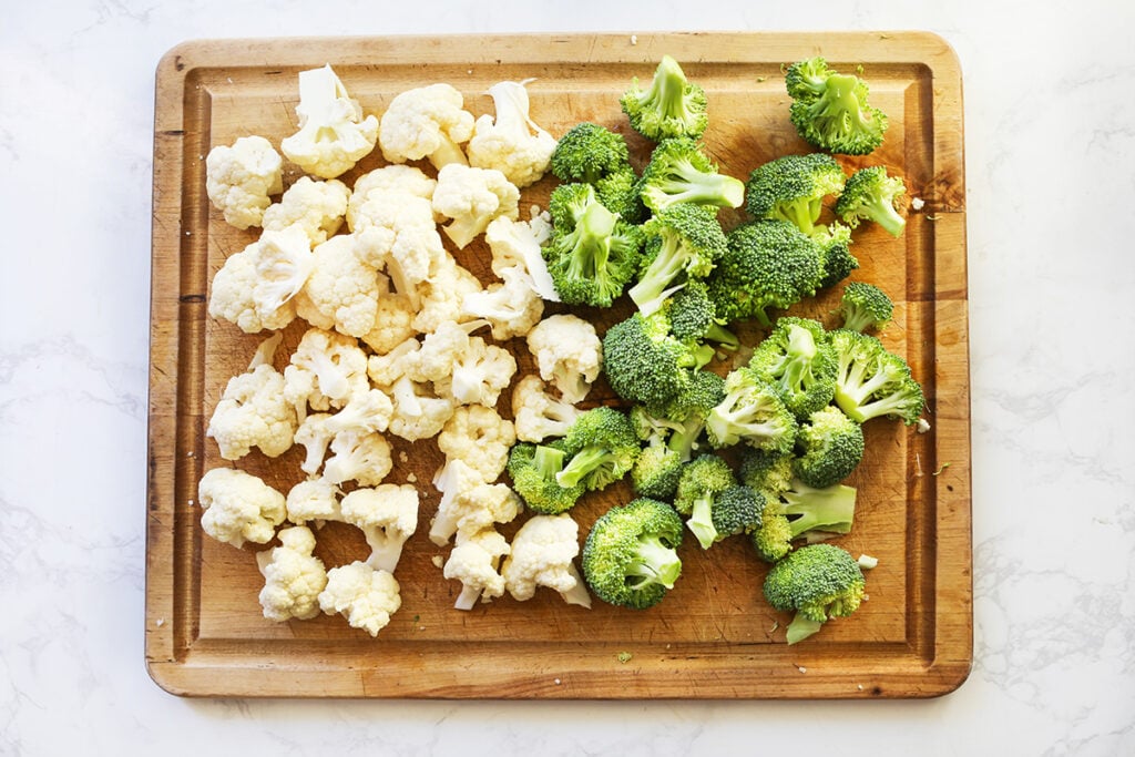 Broccoli and cauliflower florets on a cutting board in a single layer.