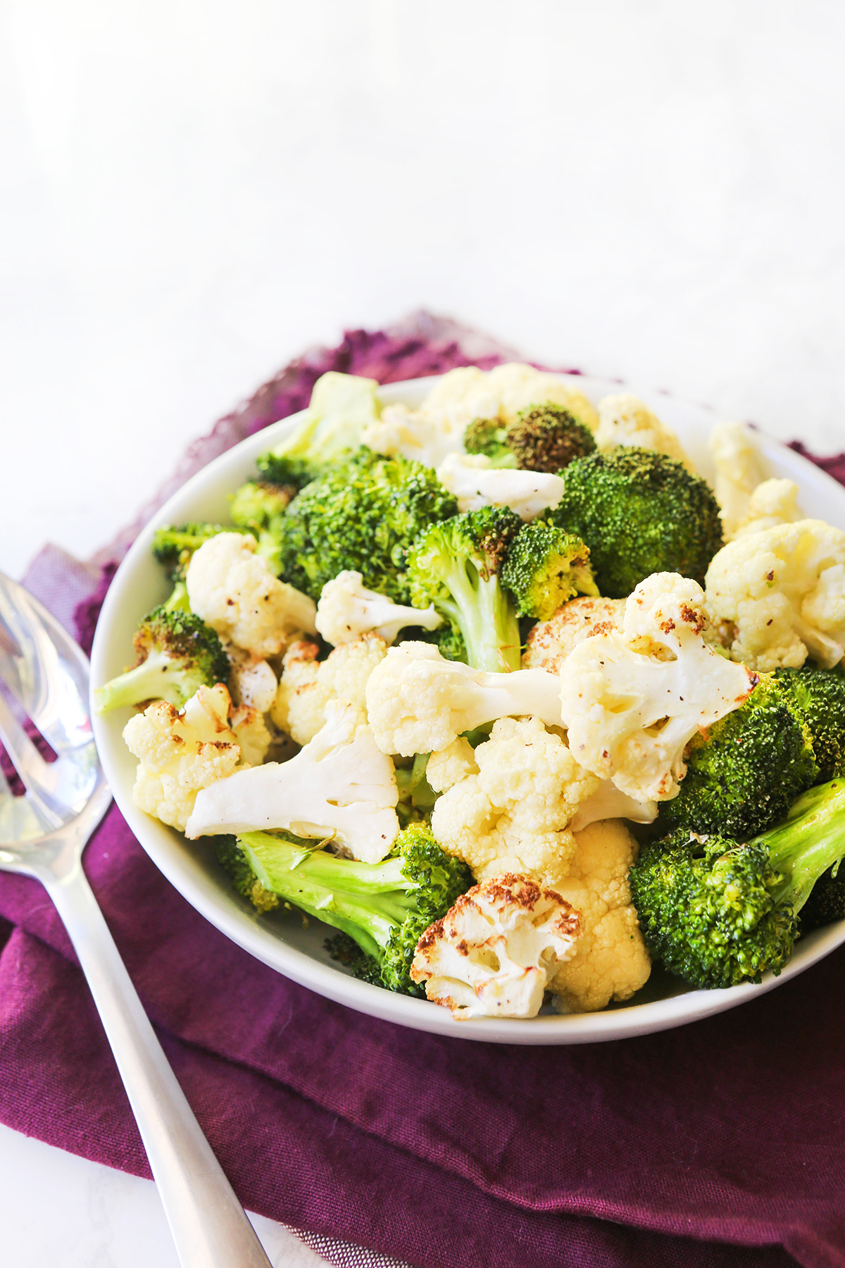 Serving bowl filled with cooked veggies, sitting next to serving spoon.