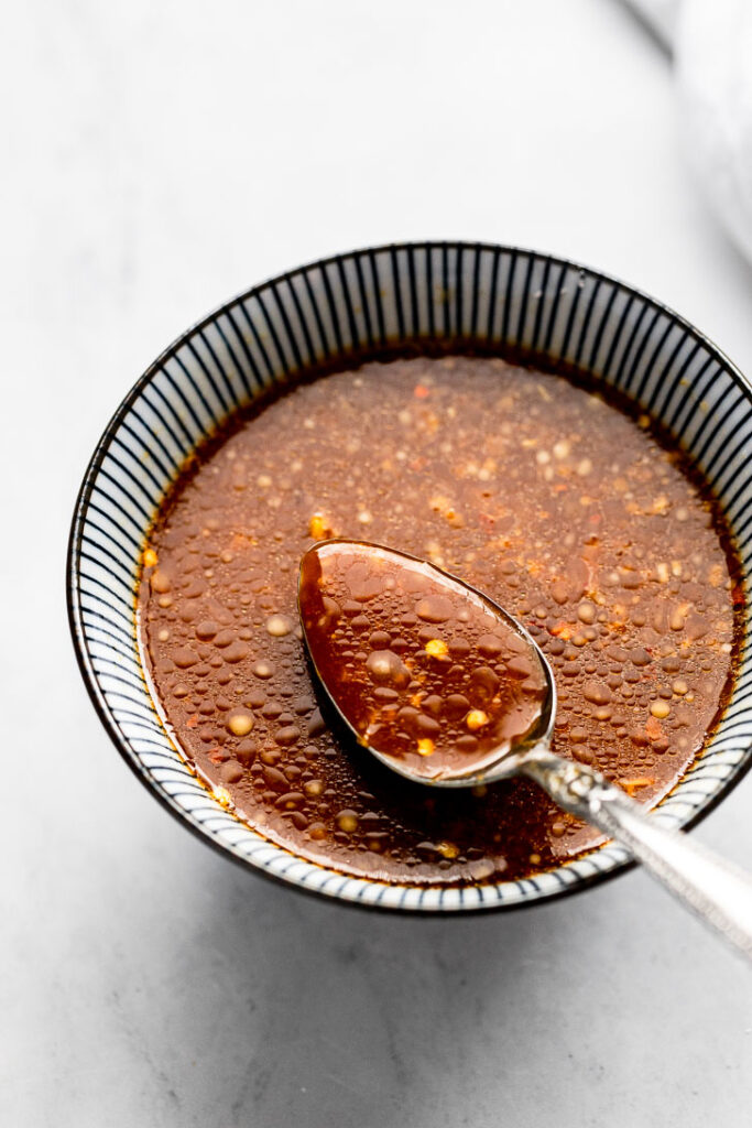 A small bowl of stir fry sauce with a spoon coming out of it. 