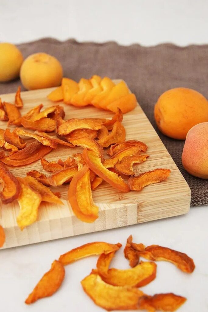 Dried apricots sitting on a cutting board next to whole apricots. 