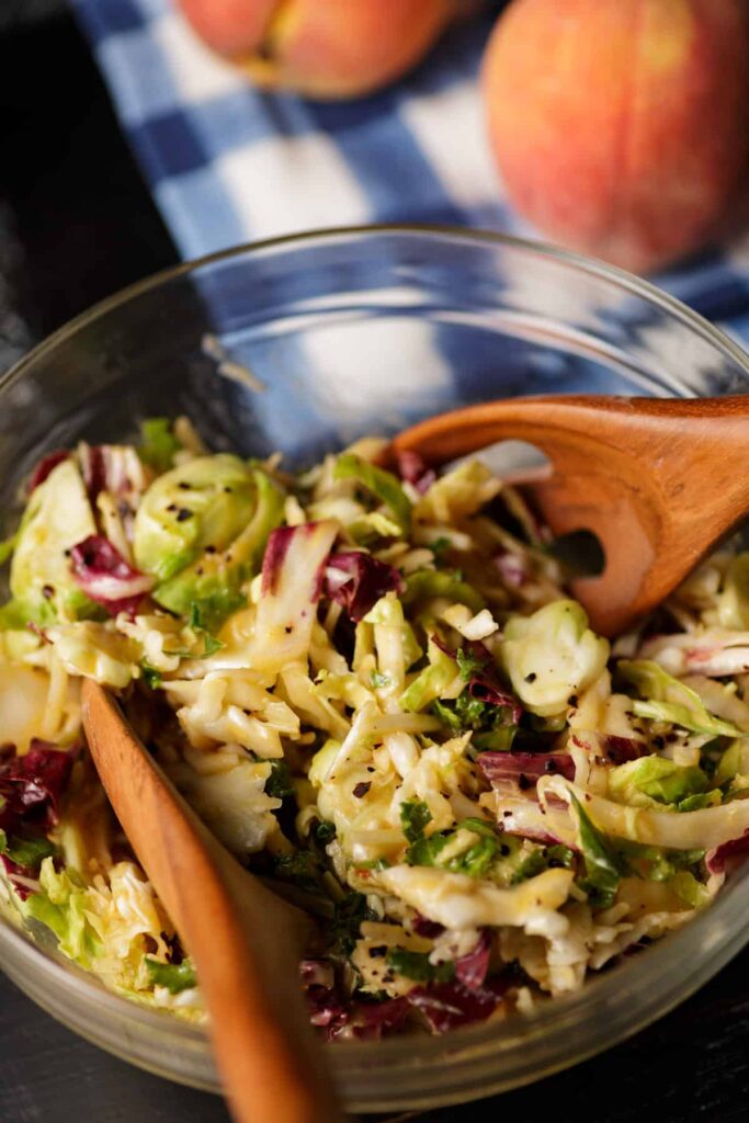 Two wooden spoons tucked into a glass bowl of peach coleslaw. 