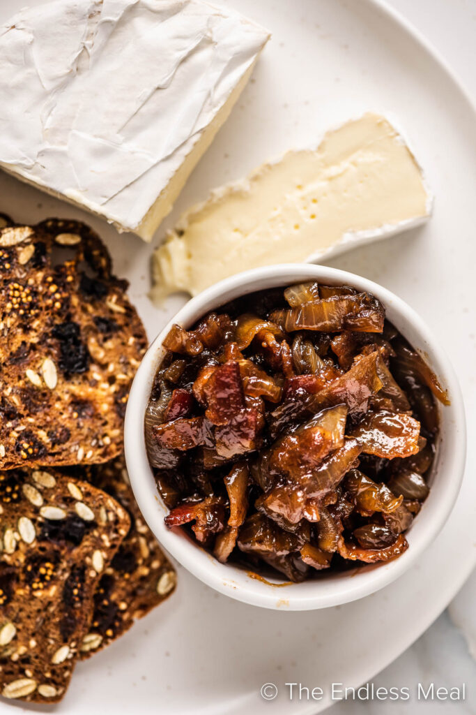 Bacon jam in a bowl with soft cheese and toasted bread slices next to it. 