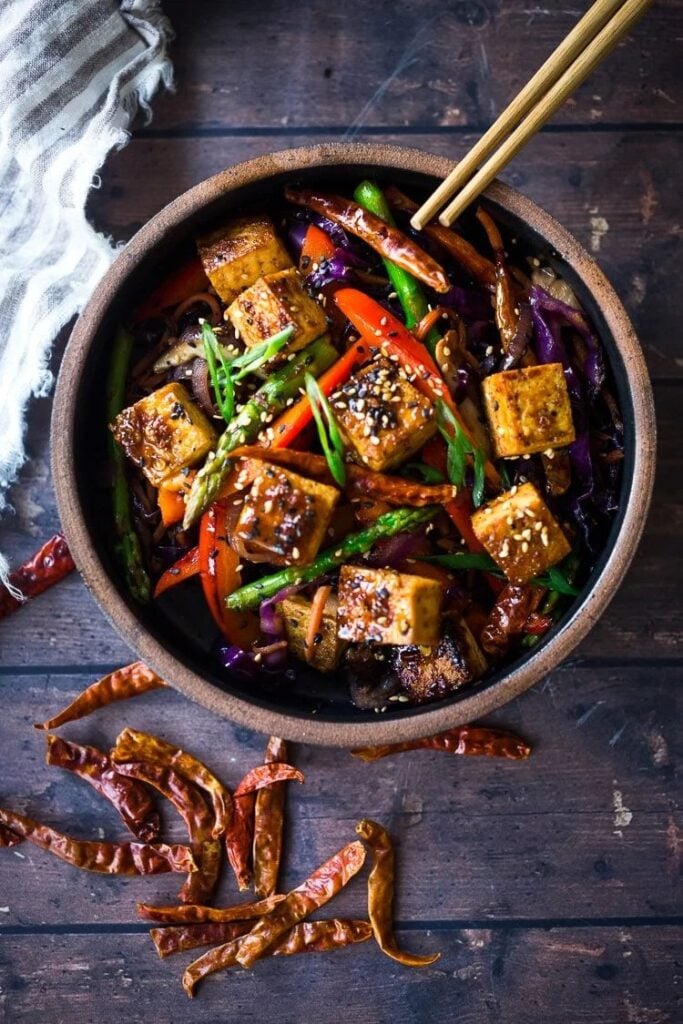 Szechuan sauce with tofu and veggies served in a wooden bowl and chopsticks. 