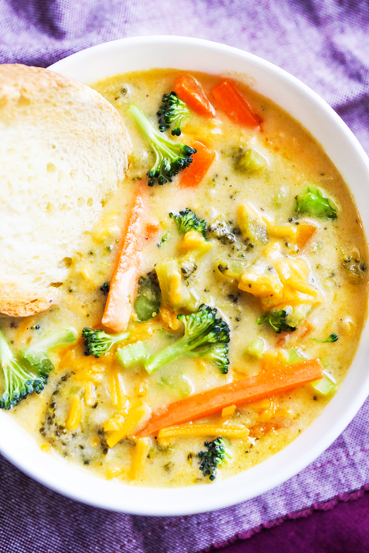 Close up top view of a bowl of broccoli cheese soup with a piece of bread tucked inside.