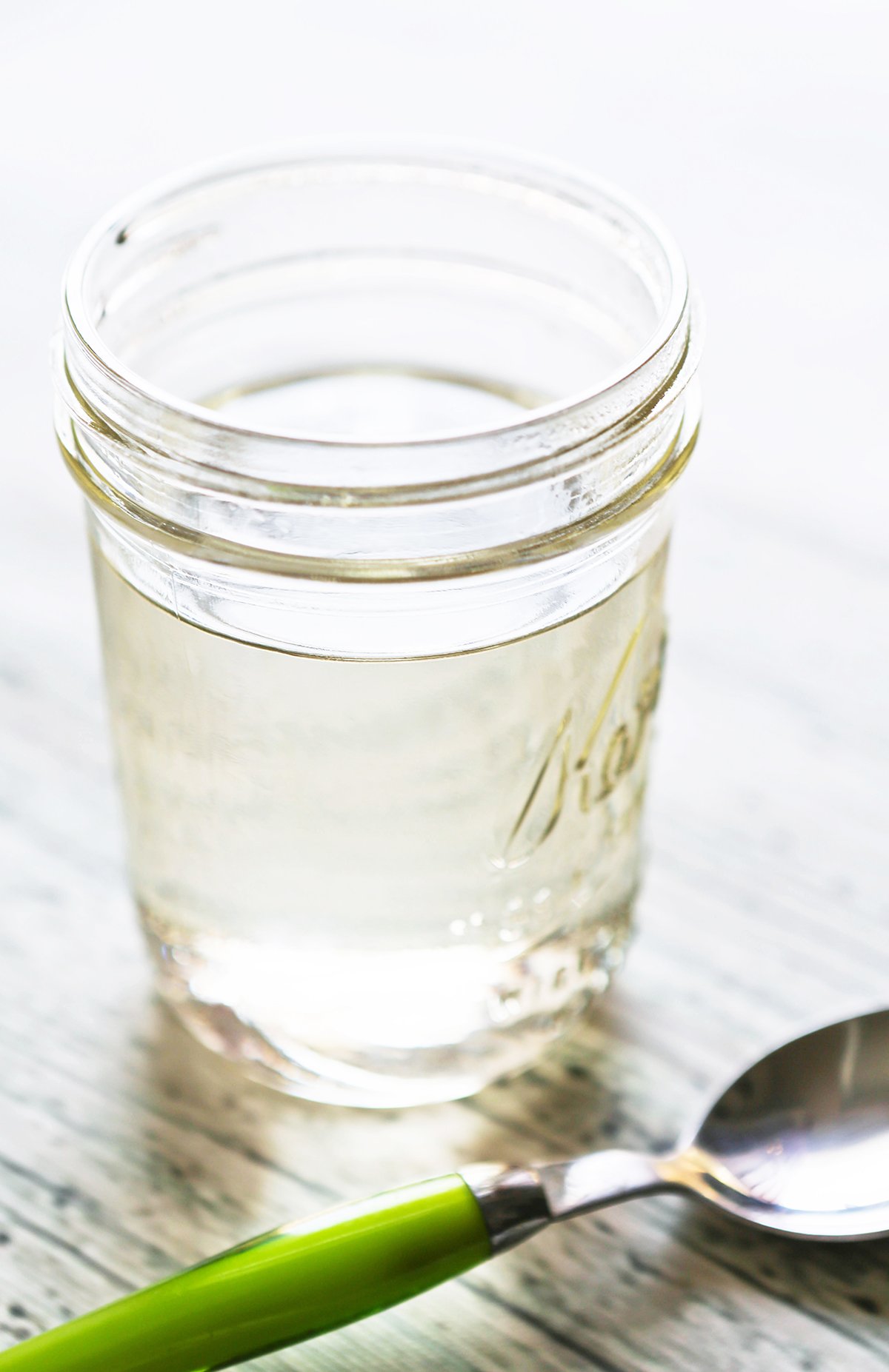 Mason jar filled with clear liquid, sitting on a counter next to a spoon.