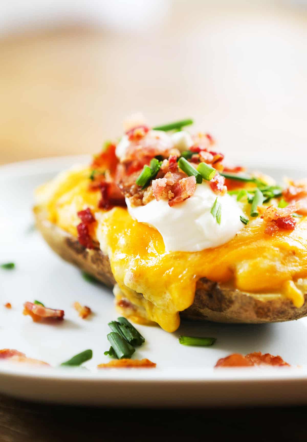 Loaded twice baked potato on a plate with cheese, sour cream and bacon piled on top.