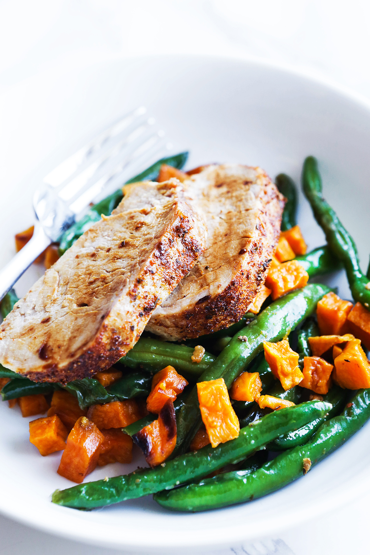 Two slices of pork on a plate with green beans and sweet potatoes.