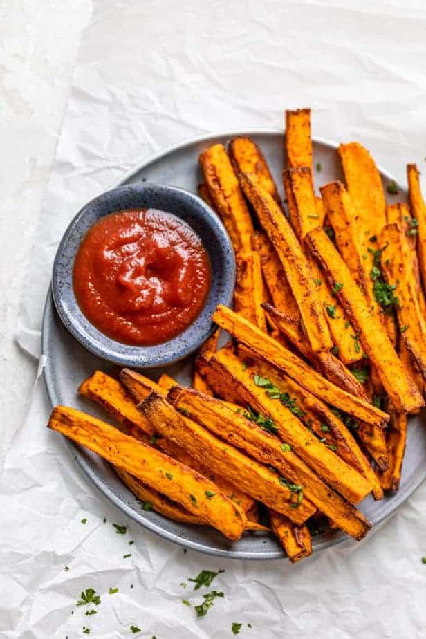 Sweet potato fries made in the air fryer on a plate with a small side of ketchup in a bowl. 