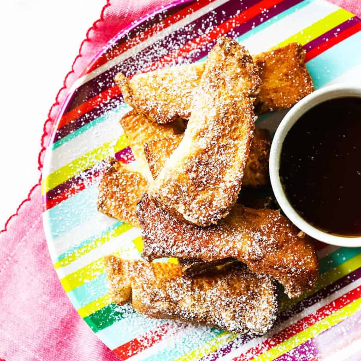 Plate of air fryer waffle strips on a plate with a small bowl of syrup. 