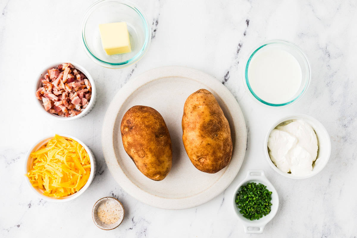 Ingredients for stuffed baked potatoes lined up on a white counter.