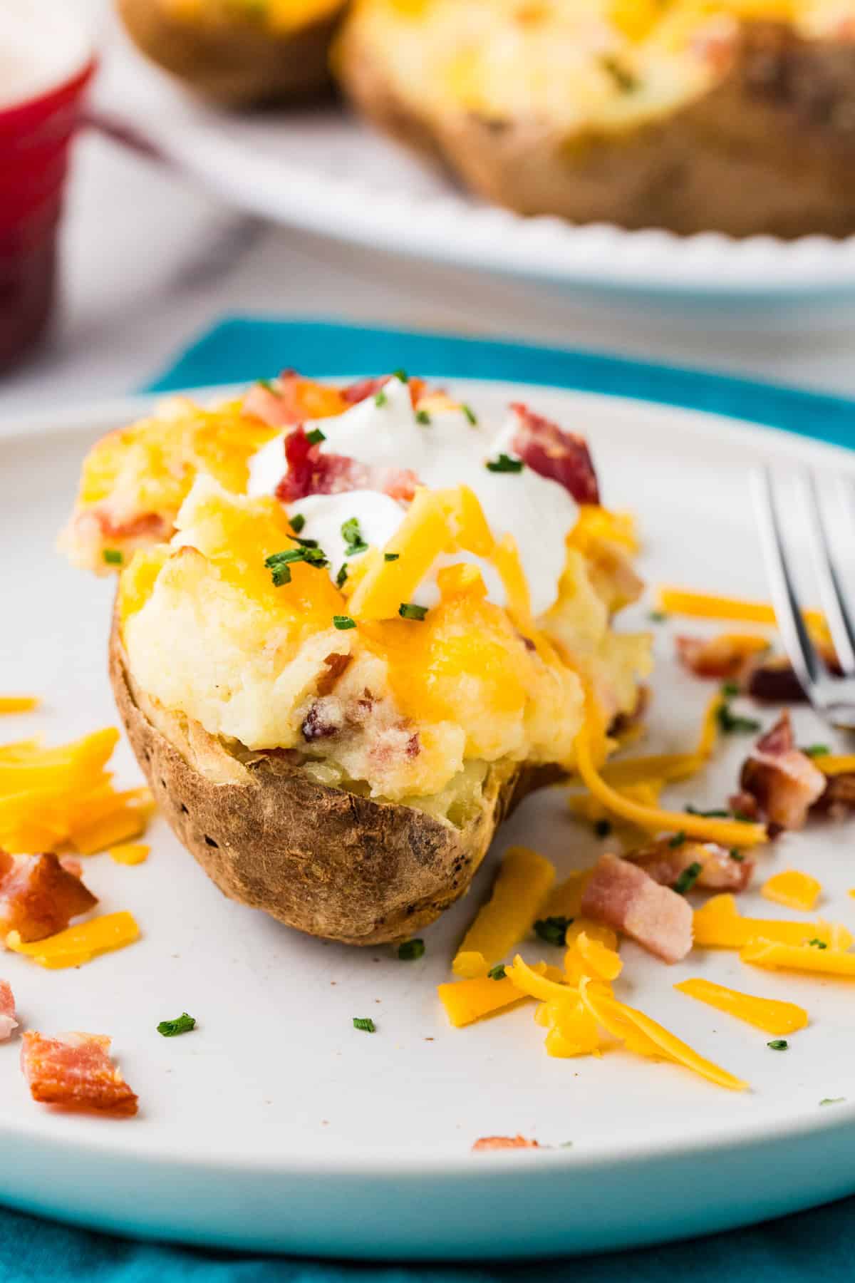 Close up of a stuffed cheesy baked potato, topped with sour cream, bacon and chives.