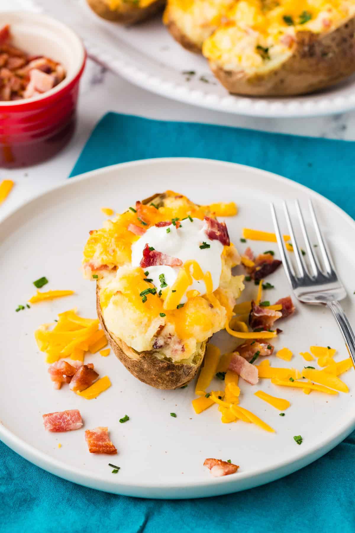 Plate with a cheesy baked potato on it, ready to eat.