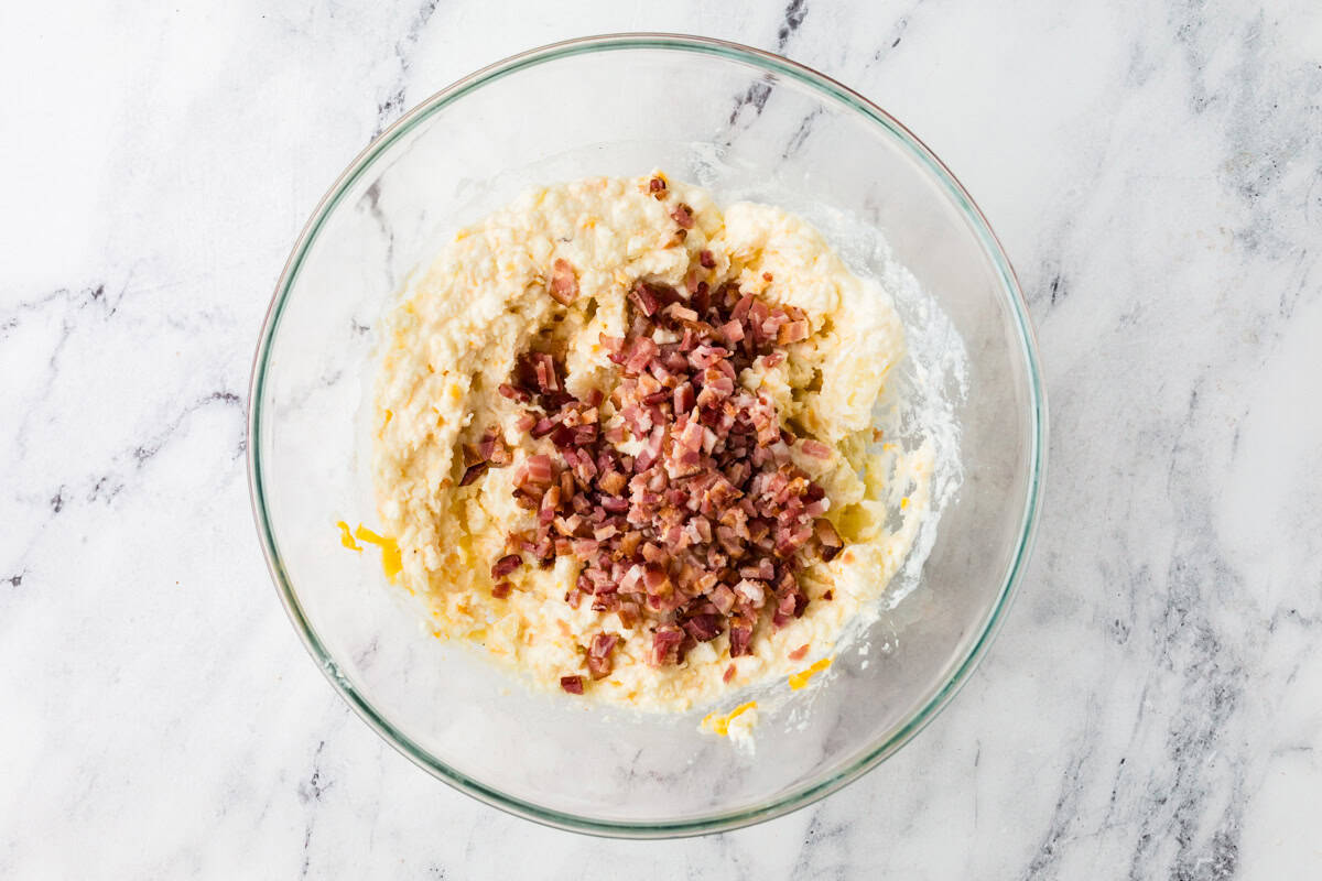 Mixing bowl with potato, cheese and bacon pieces, all mixed together.