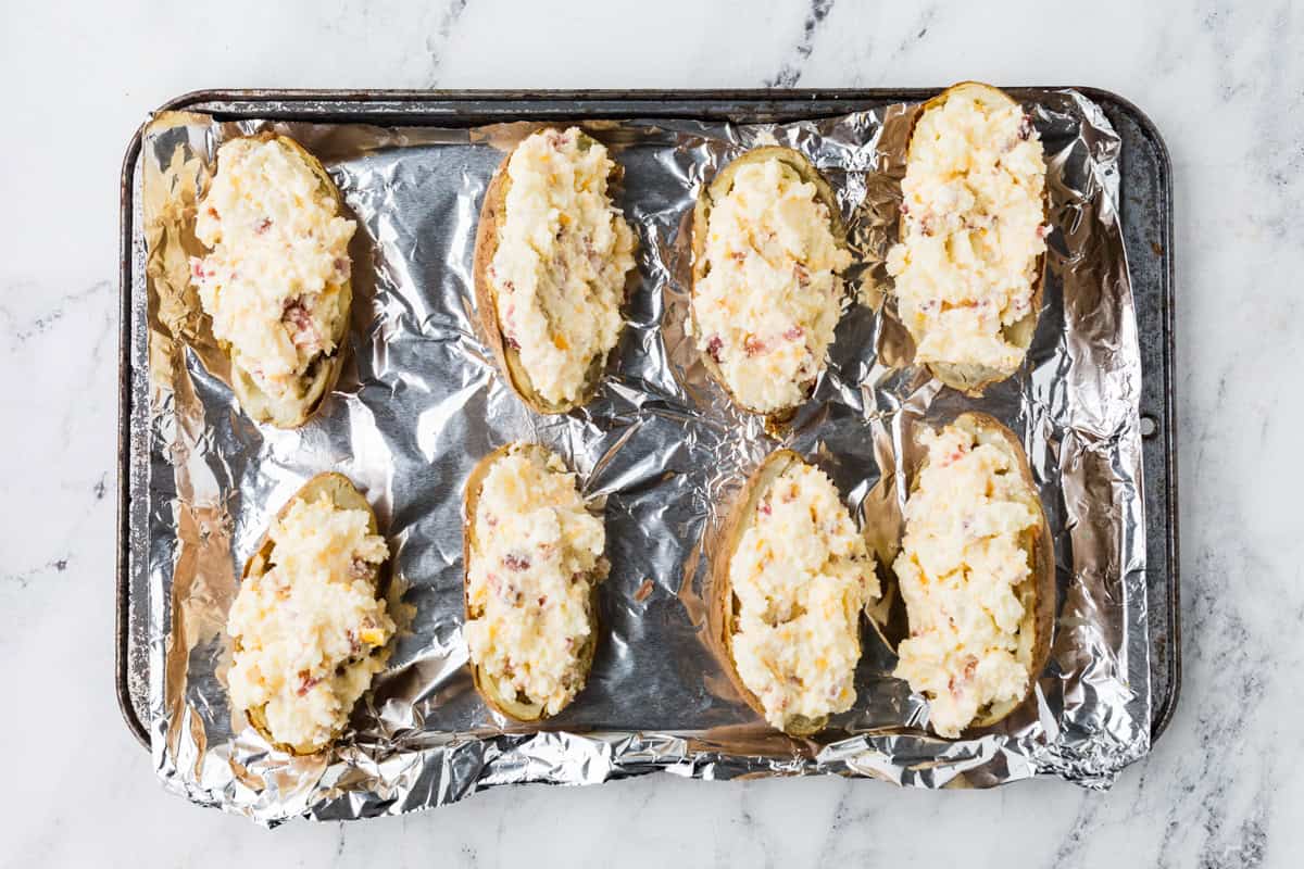 Baking sheet with eight baked potato halves, each filled with a filling.