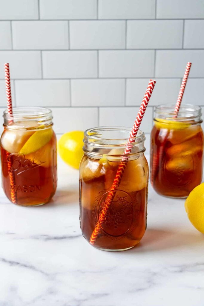 3 Mason jars of earl grey ice tea with lemon wedges and a paper straw inside. 