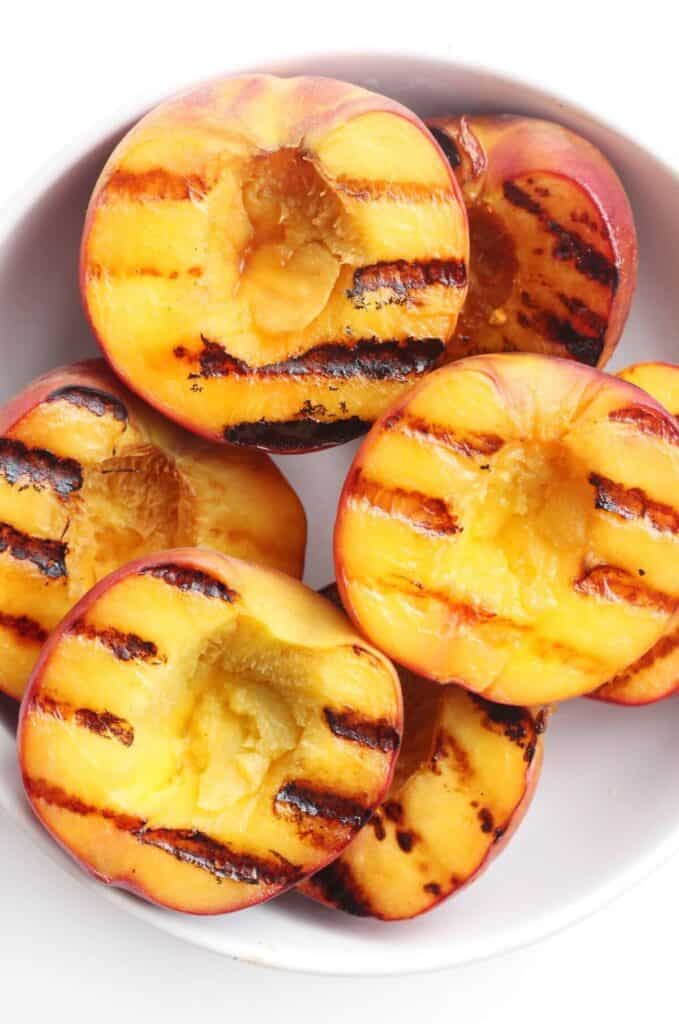 Halved peaches that were grilled and placed in a bowl. 