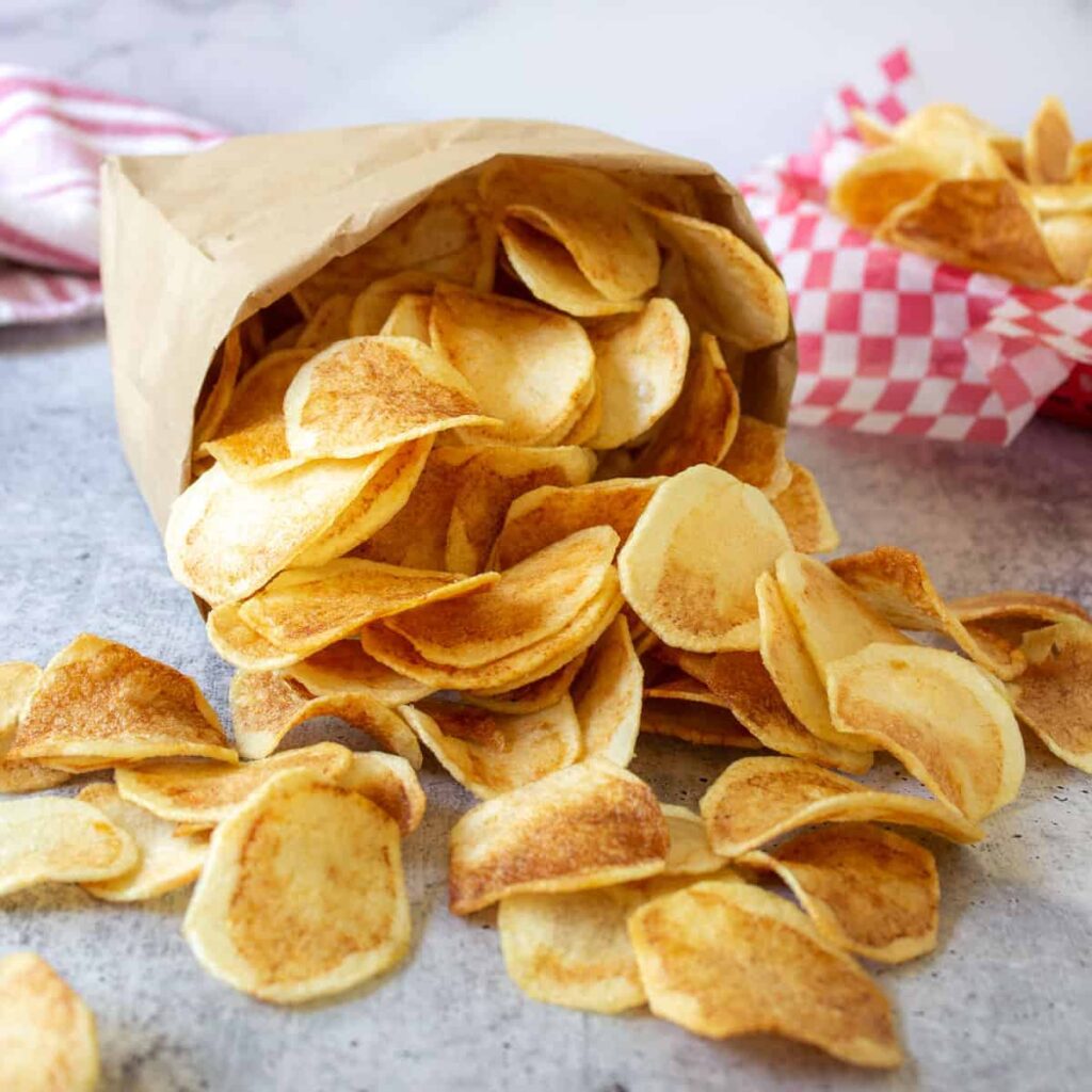 Paper bags on its side with homemade potato chips spilling out. 