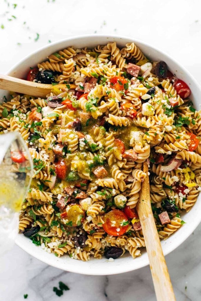 Large serving bowl of easy pasta salad with wooden salad tongs. 