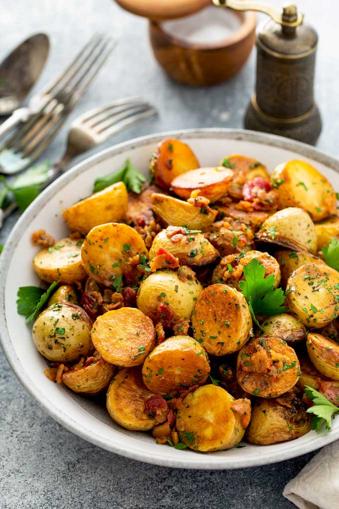 Bowl of crispy skillet potatoes with crispy bacon pieces and herbs.