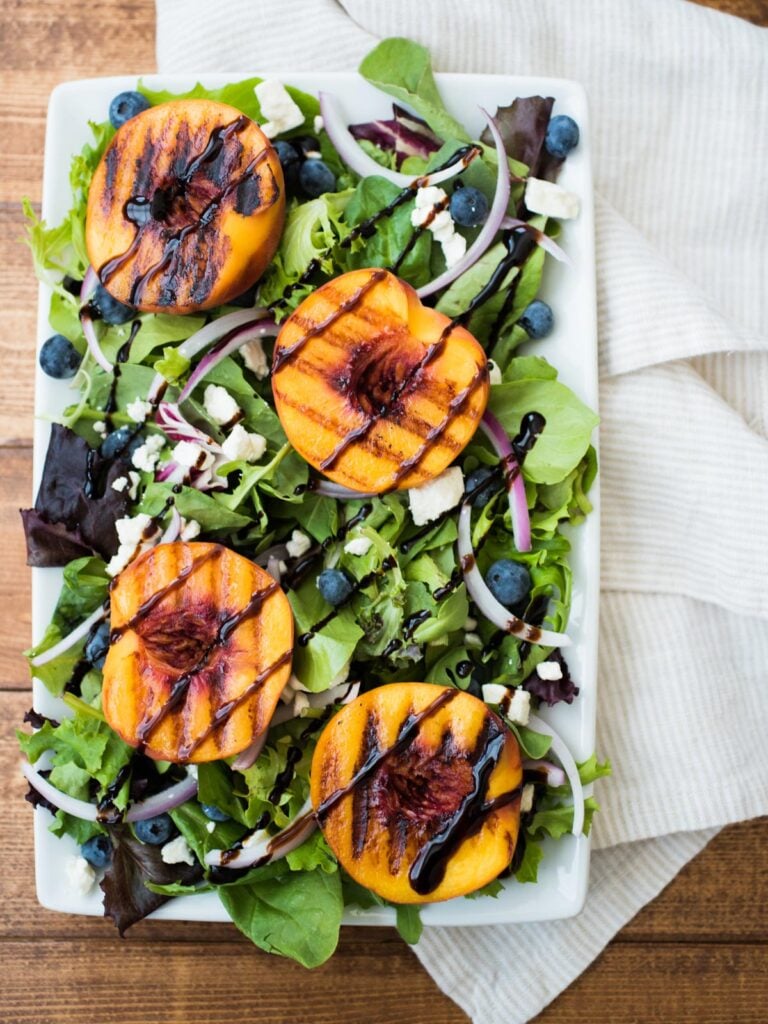 Grilled peach salad with a dressing drizzled over the top on a rectangular white serving plate. 