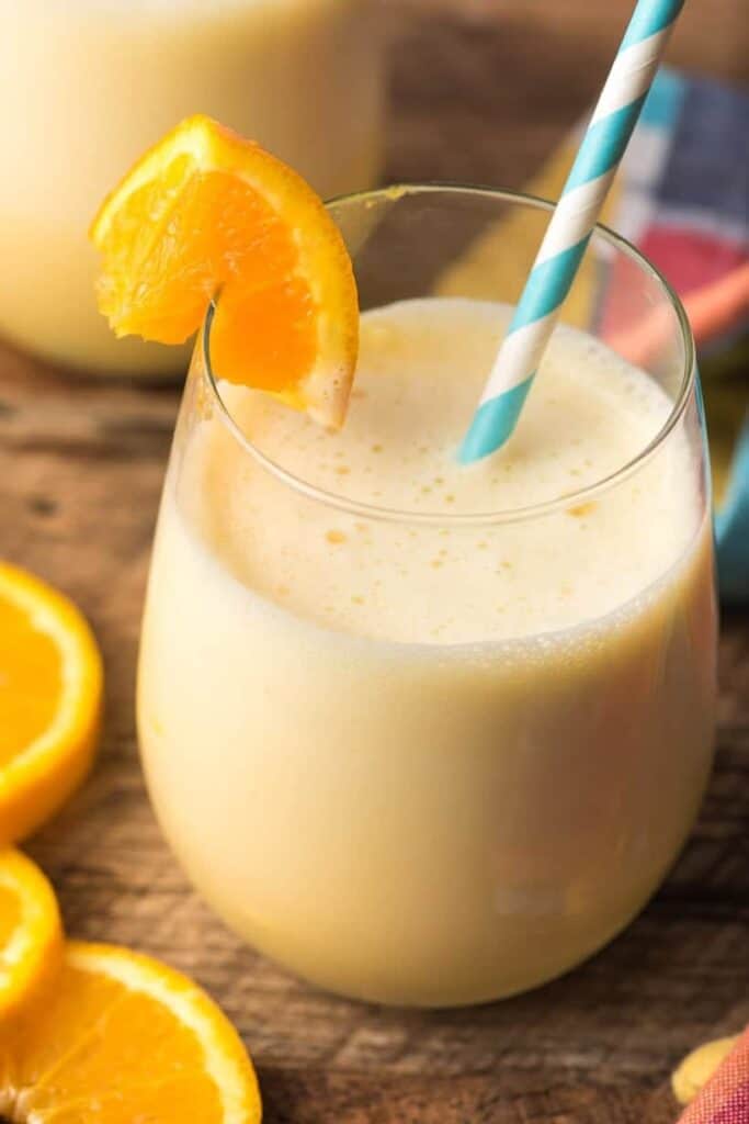 Glass of orange julius with a paper straw and an orange garnish. 