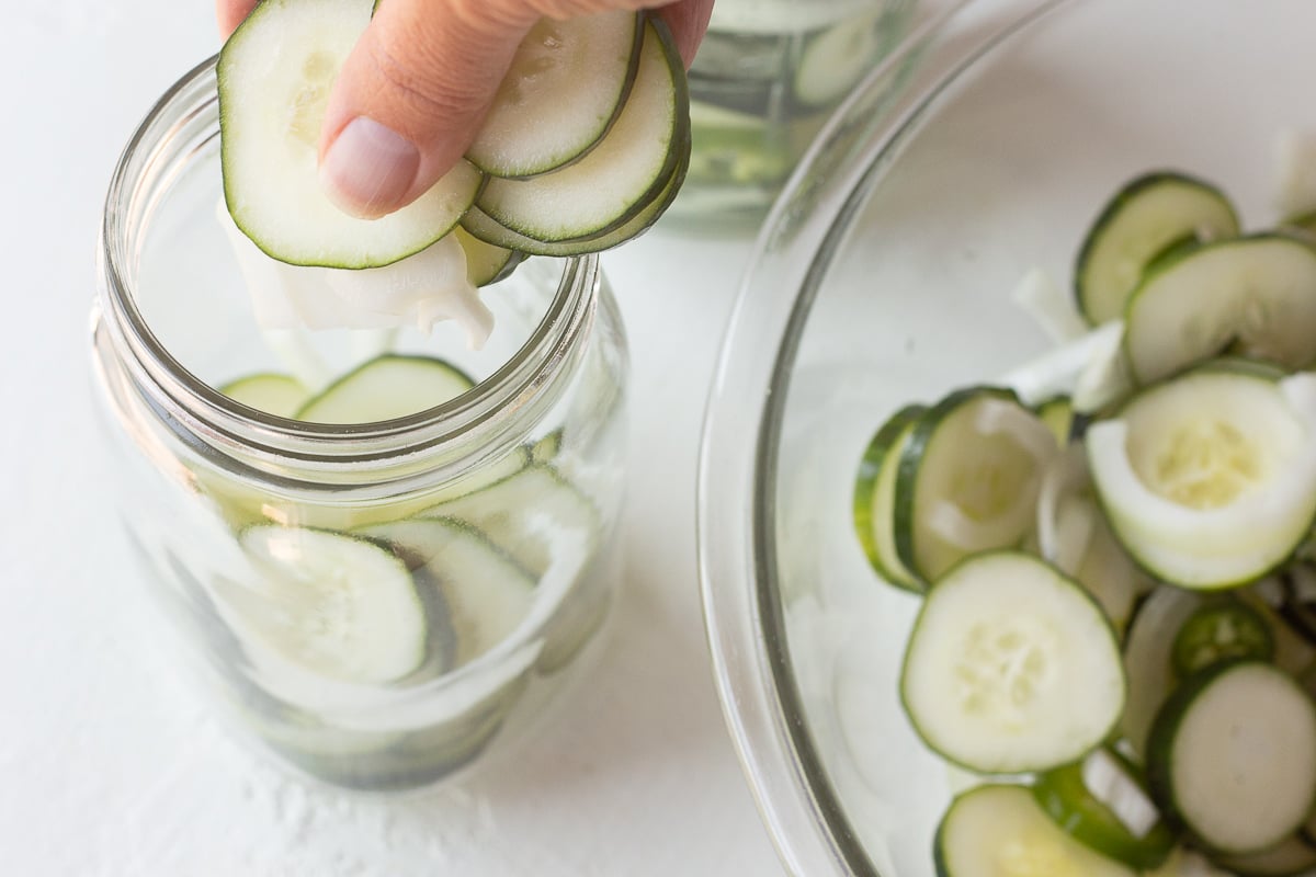 Hand dropping sliced cucumbers into a mason jar.