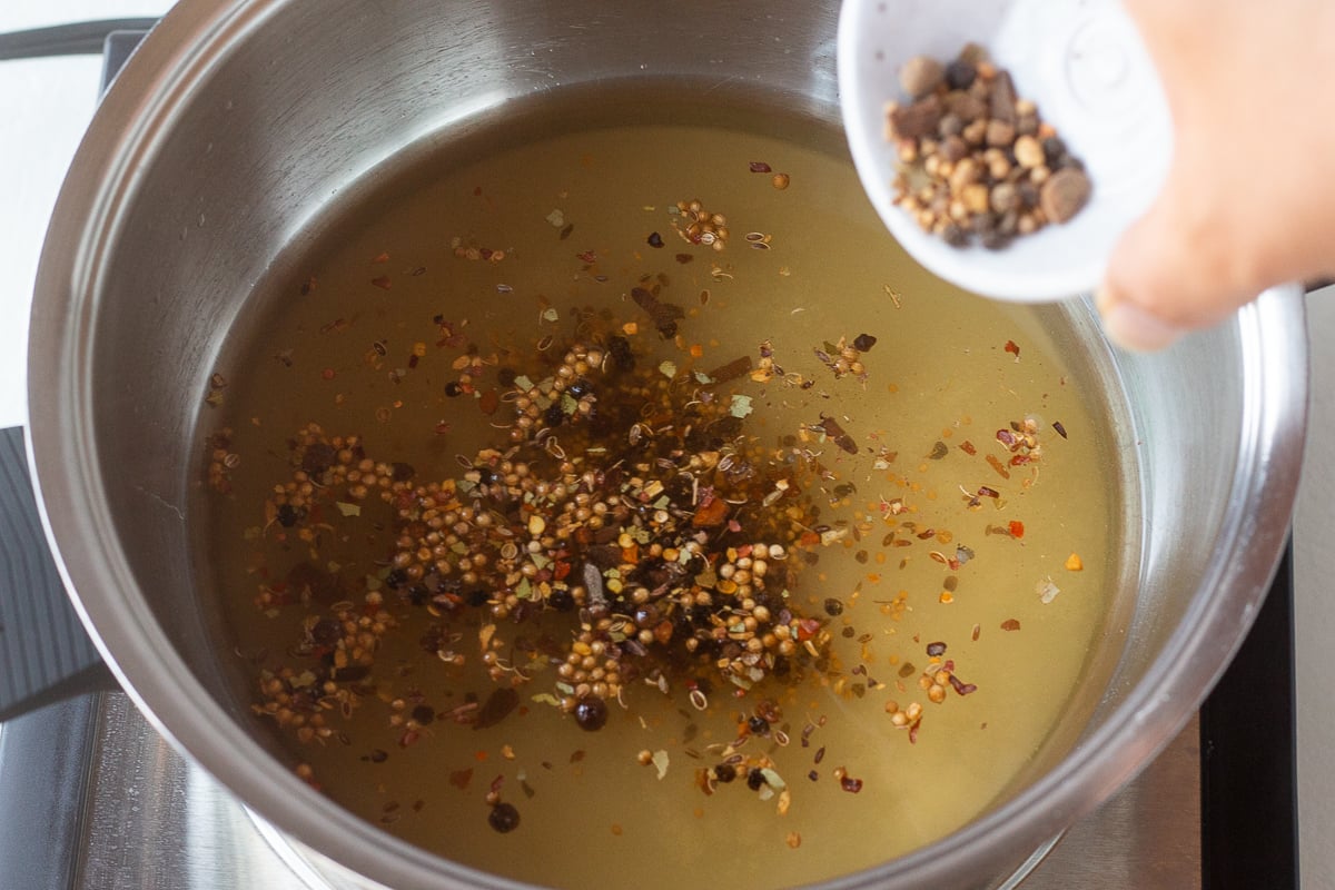 Pickling spices being added to a saucepan with liquid.