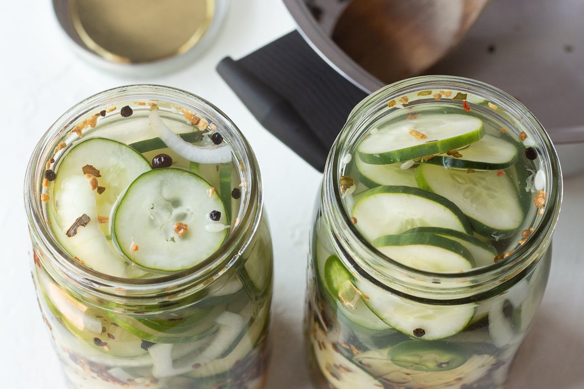 Two mason jars filled with cucumbers, onions, spices and vinegar.