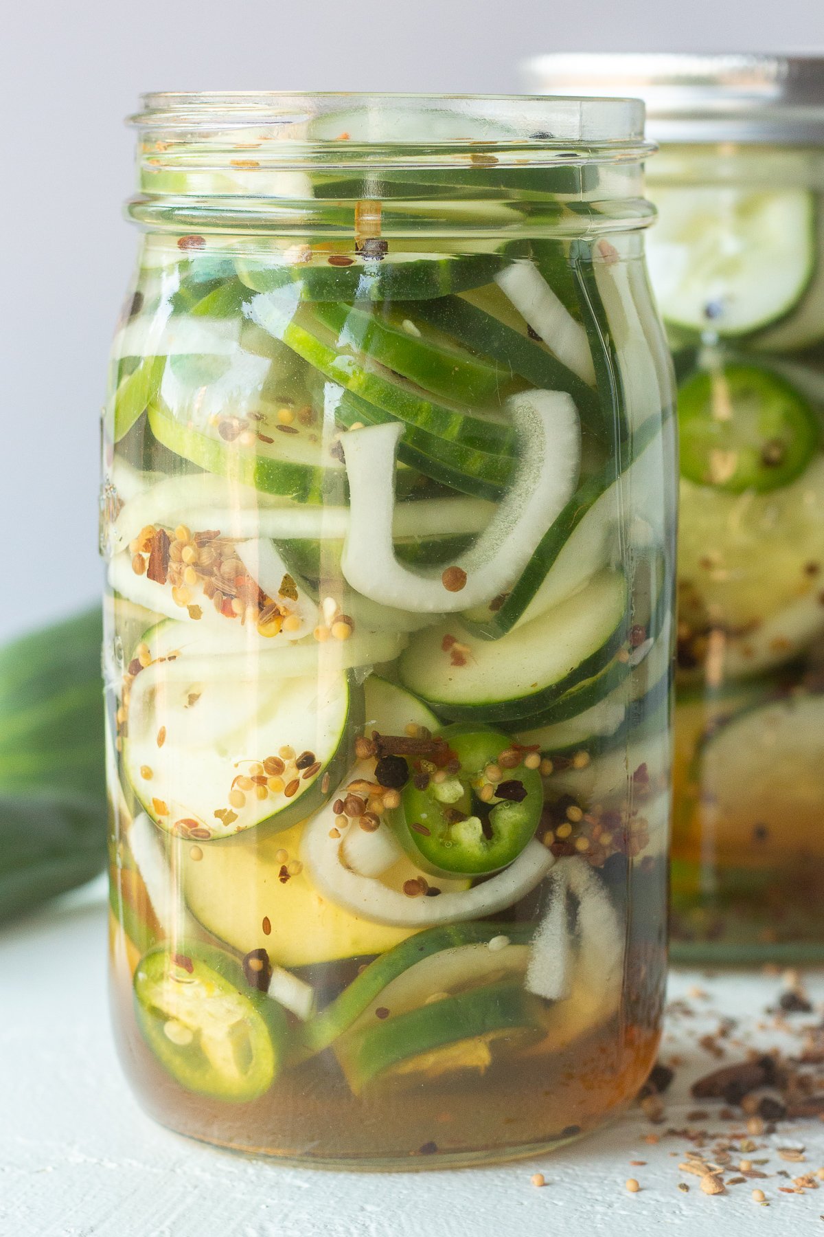 Side view of a mason jar filled with sliced cucumbers, liquid and onions.
