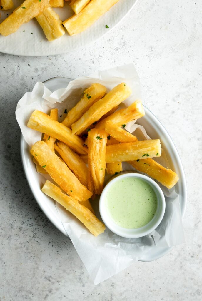 Yuca frieds in a container with a small bowl of dipping sauce. 