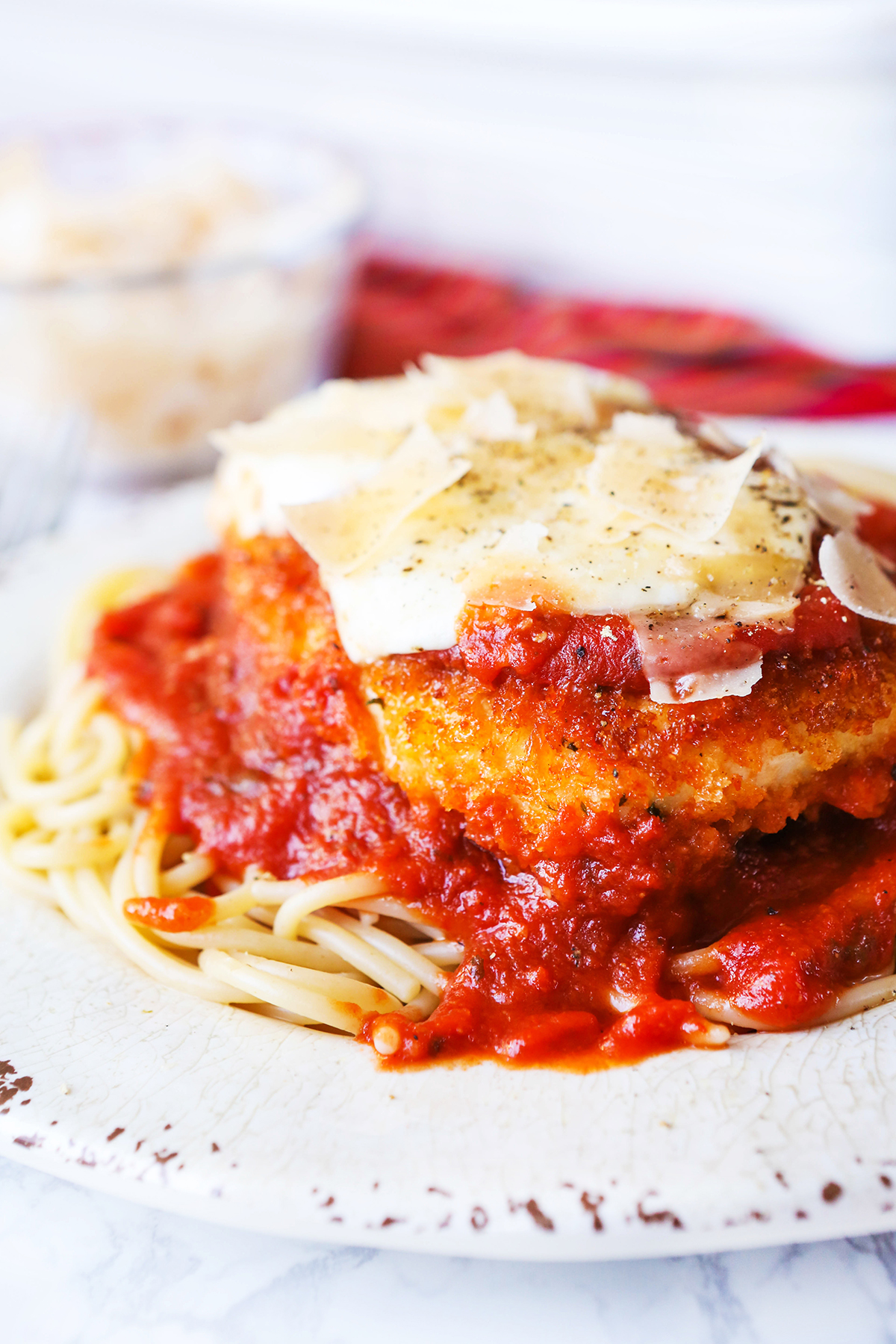 Chicken parmesan on a plate served over noodles and topped with shaved cheese.