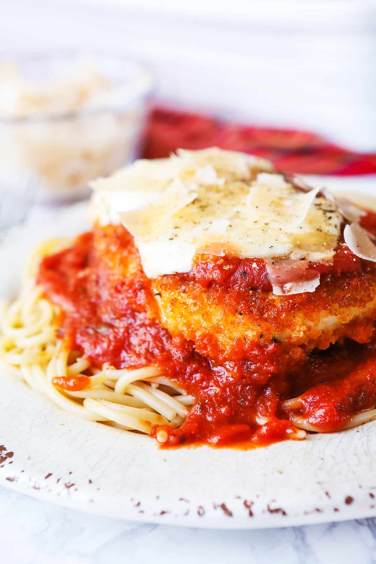 Chicken parmesan over spaghetti noodles on a plate and with shaved parmesan on top.