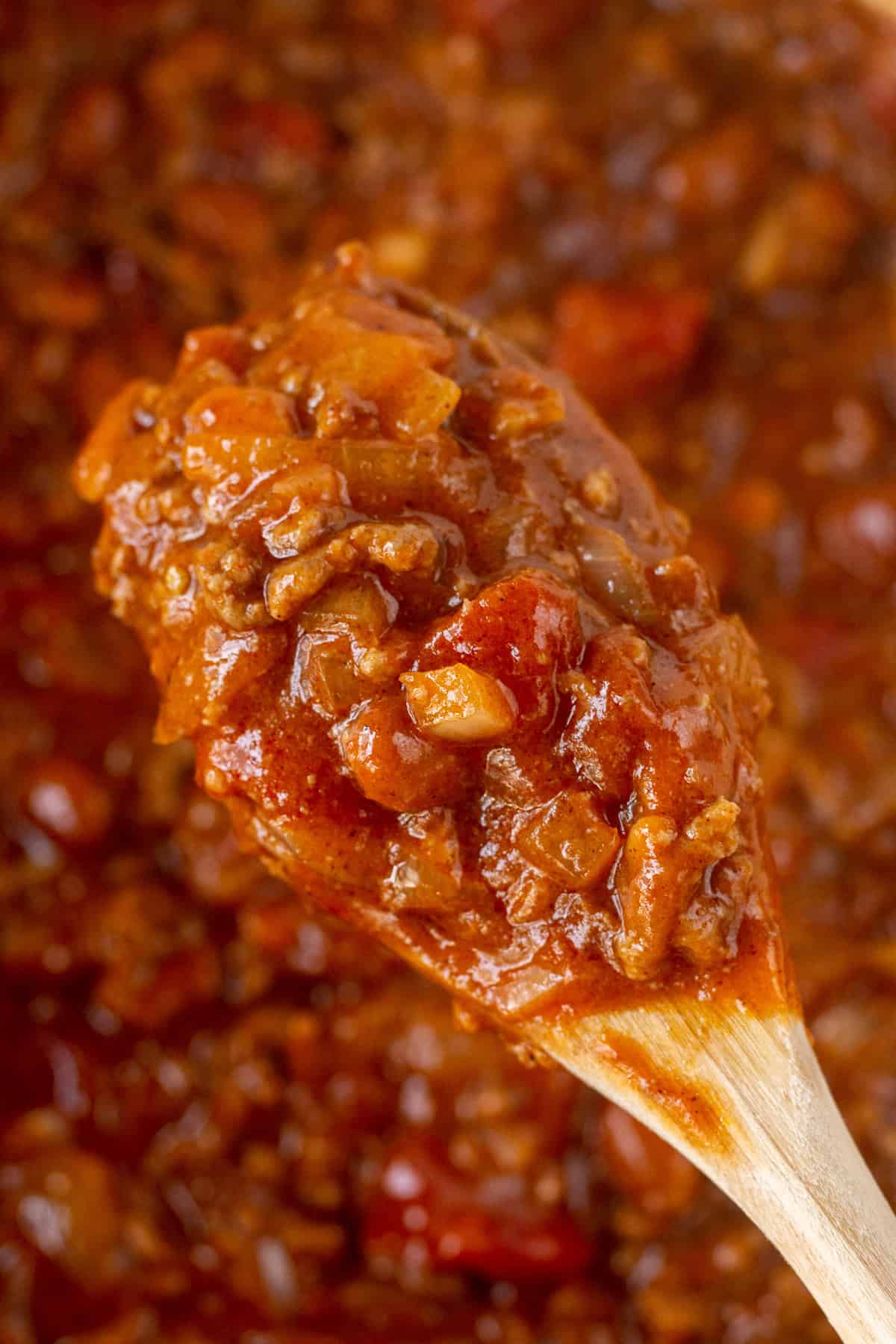 Wooden spoon holding heaping spoonful of chili over a Dutch oven.