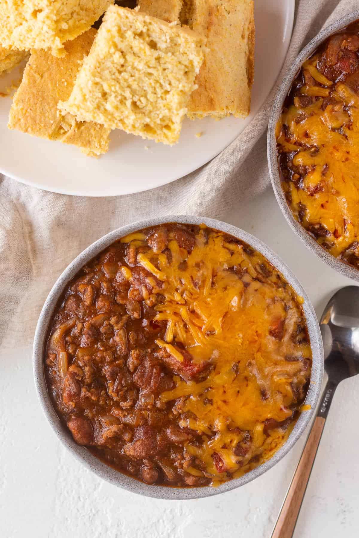 Top view of two bowls of chili covered with melted cheese.