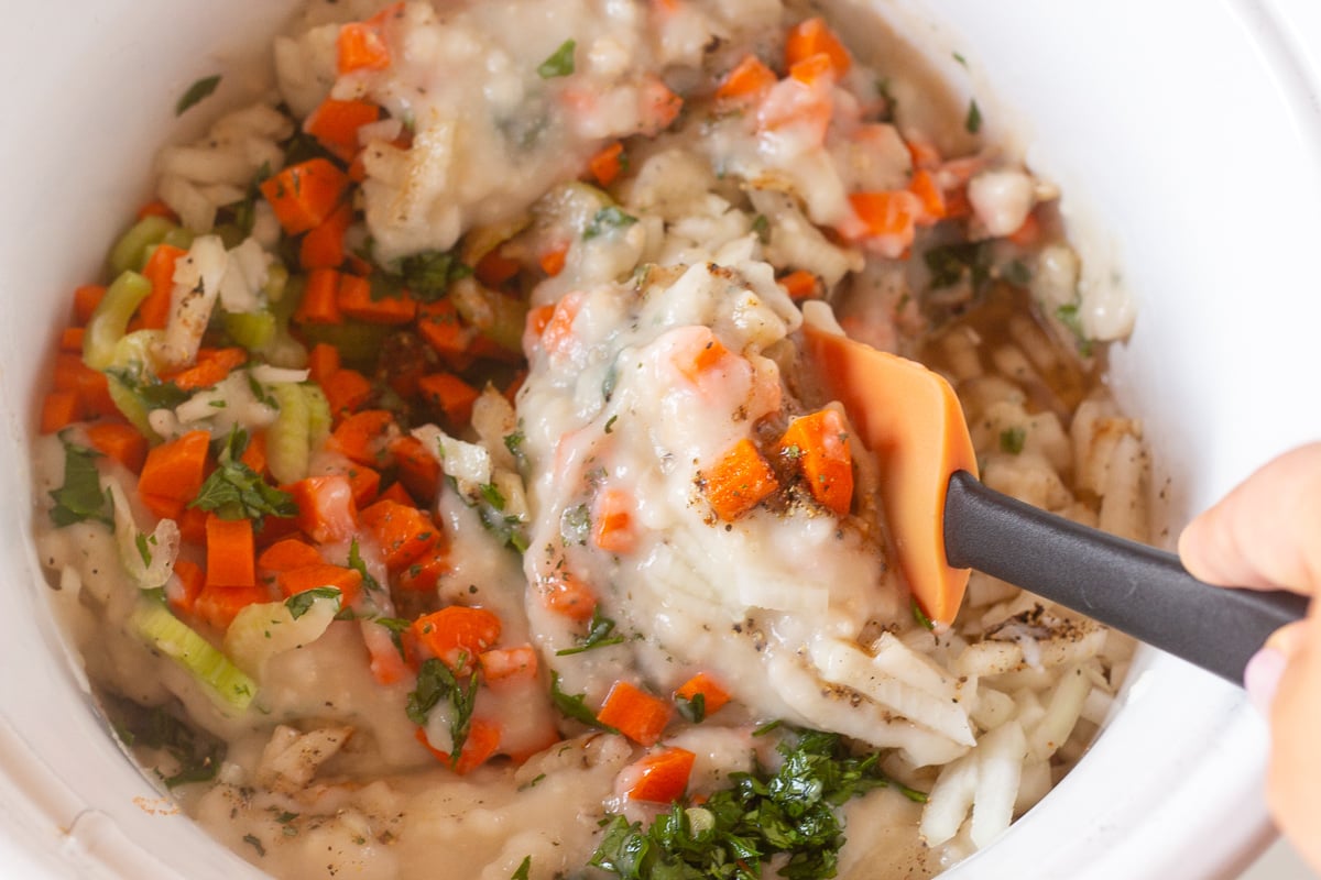 Spatula stirring veggies and creamy soup in a crockpot.