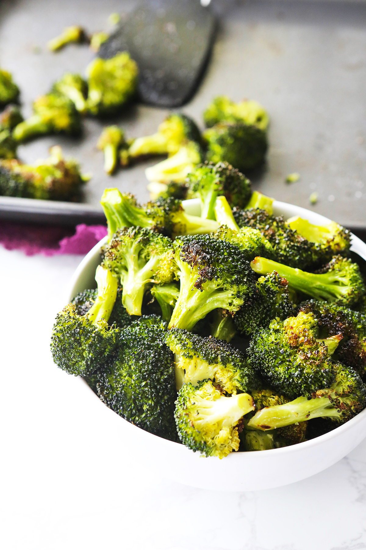 Roasted broccoli in a bowl next to a baking sheet.