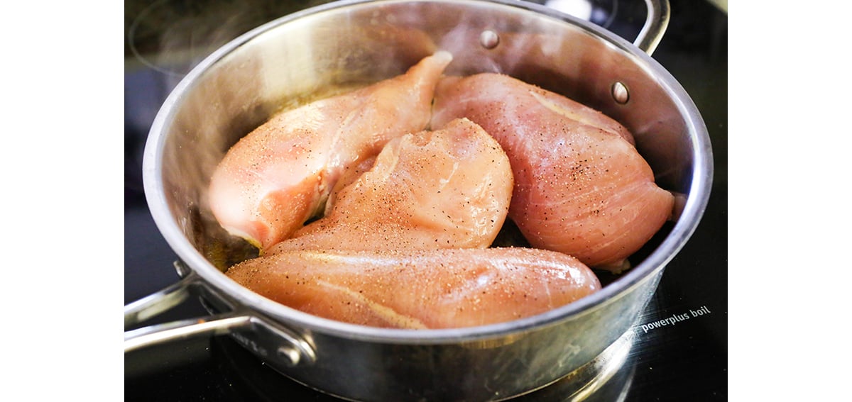 Skillet packed full of uncooked chicken breasts.