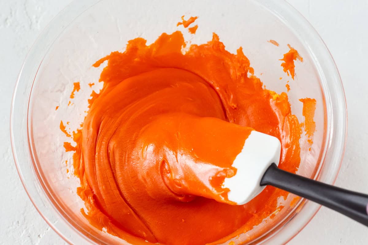 Creamy orange caramel mixture in a glass bowl with spatula.