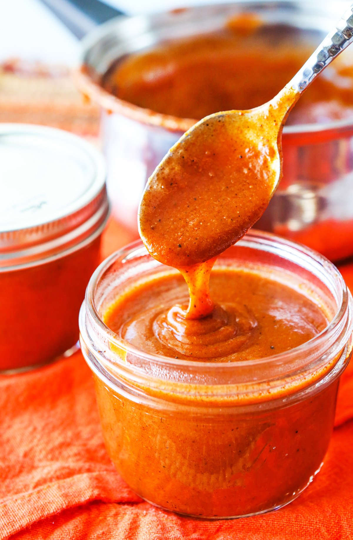 Enchilada sauce drizzling off a spoon into a jar filled with the red sauce.