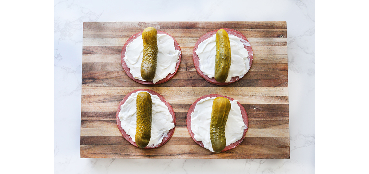 cutting board with corned beef, cream cheese and pickles stacked.