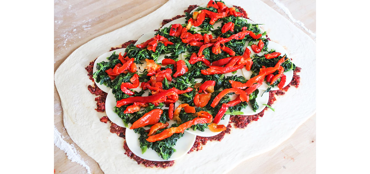Layers on top of pizza dough, including peppers, spinach and cheese.