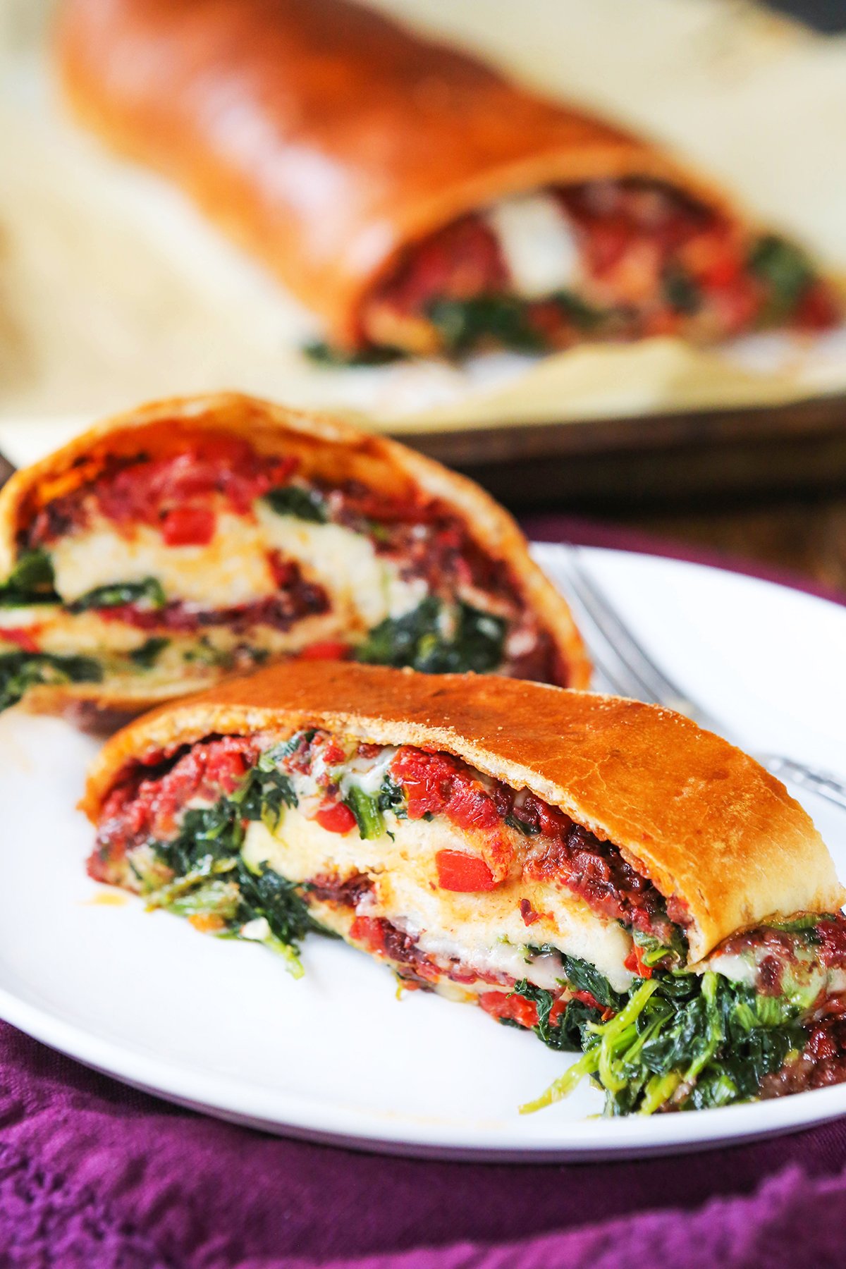 Two slices of stromboli on a plate, with cheese, tomatoes and spinach coming out the sides.