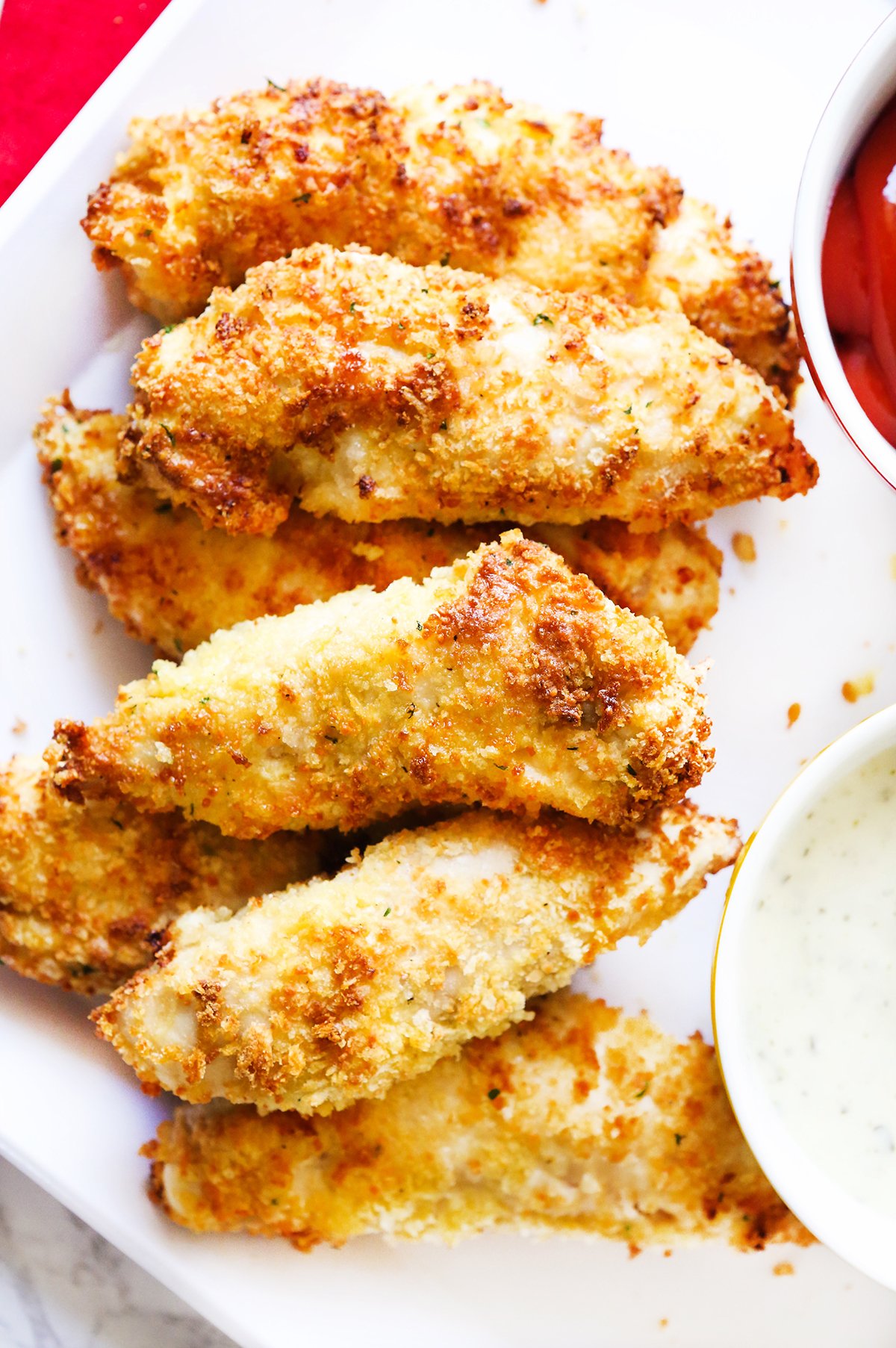 Crispy chicken tenders lined up on a serving plate with dipping sauces tucked in.