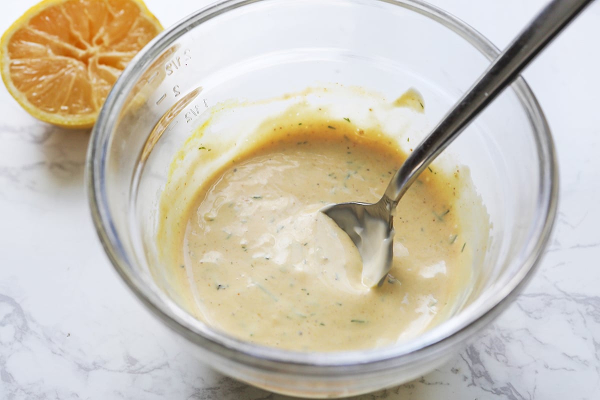 Creamy sauce with dill in a mixing bowl with a spoon.