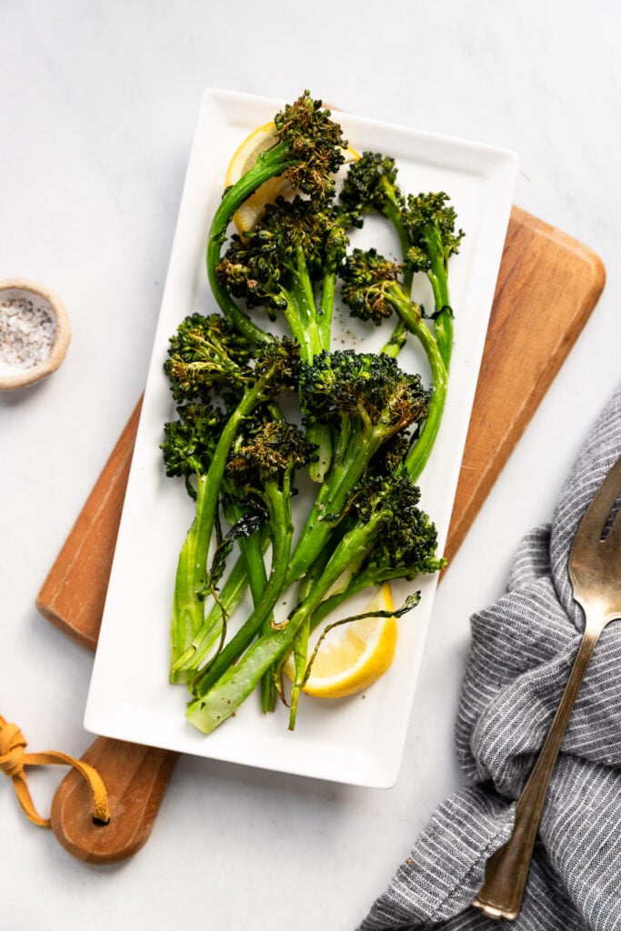 Air Fryer broccolini on  a rectangular serving platter with a lemon wedge. 