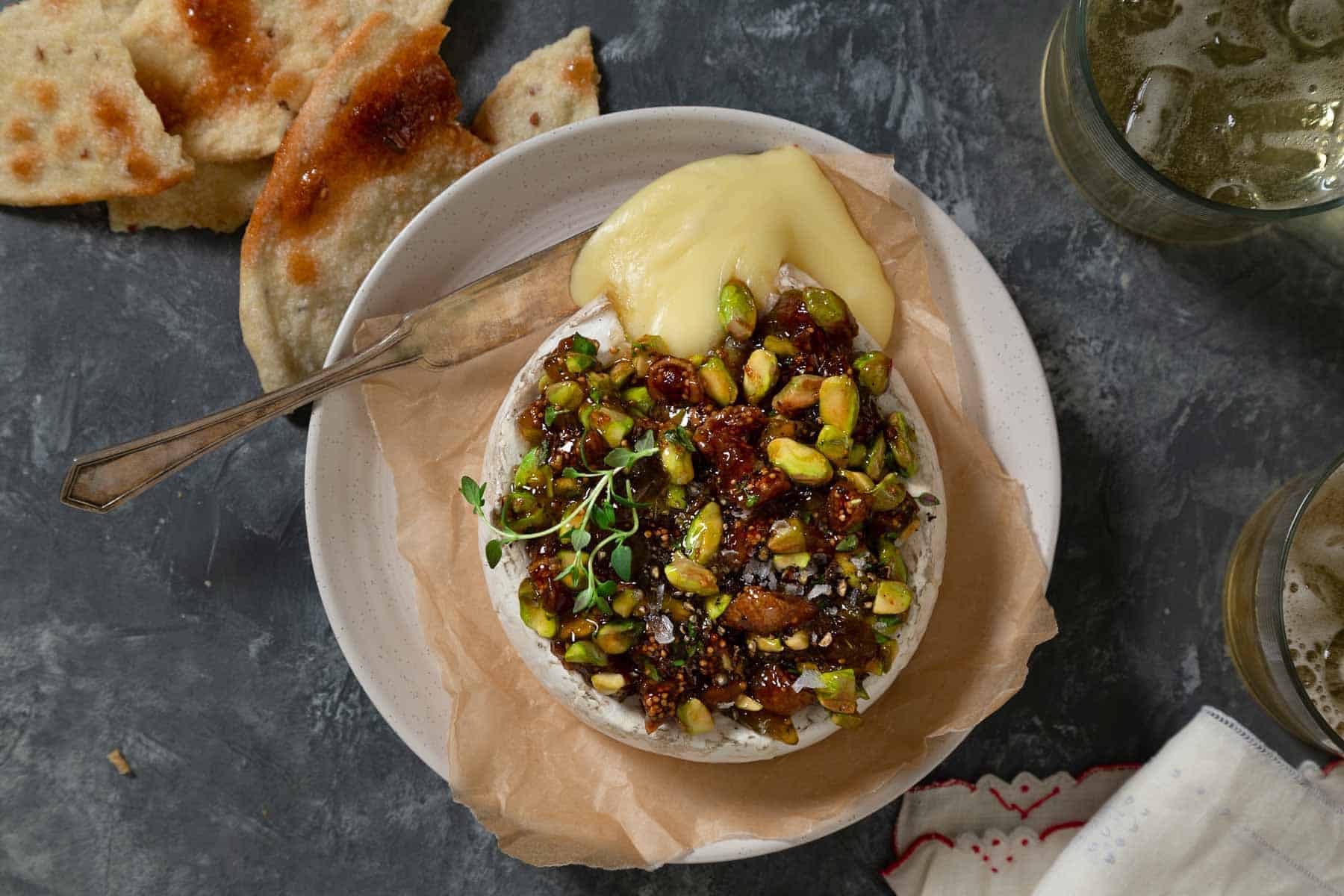 Baked brie with fig jam and pistachios melting onto a plate. 